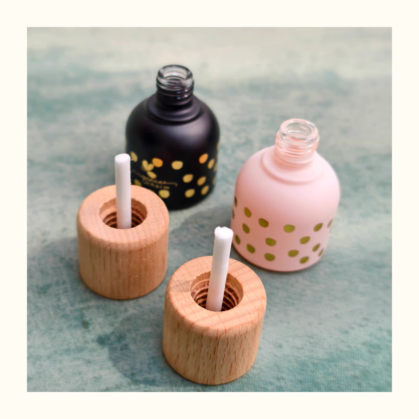 Two wooden candle holders with candles inside, next to two nail polish bottles on a textured surface.