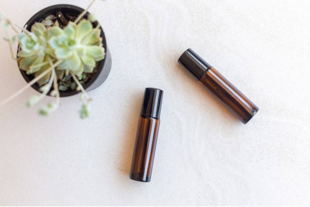 Two brown roller bottles on a white surface with a small succulent plant.